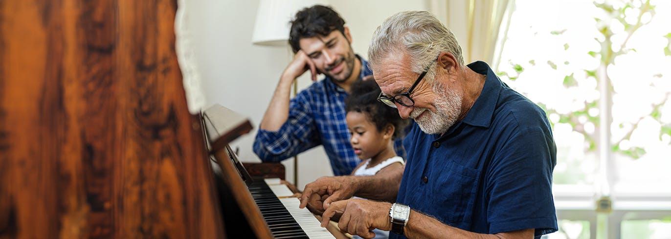 Un grand-père apprend à sa petite fille à jouer du piano pendant que son père les regarde.